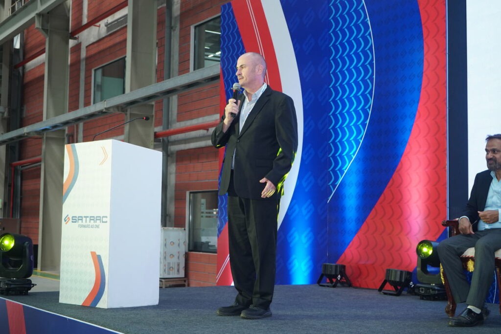 Speaker on a lit stage beside a branded lectern at a Satrac event in Chennai
